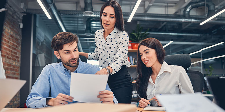 Jeune femme cheveux brun long devant deux collaborateurs un homme et une femme, travaille dans le développement durable et la gestion de projet digitale