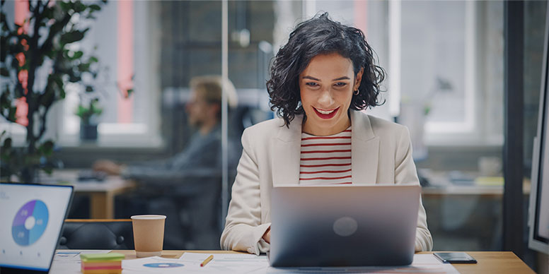 Jeune femme cheveux brun court devant son ordinateur qui sourit, travaille dans le développement durable et la gestion de projet digitale