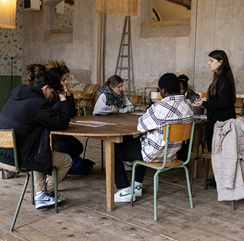 Table rond d'étudiants qui écoutent leur intervenant debout face à eux